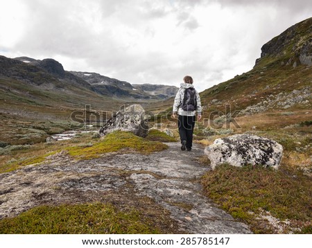 Woman alone walking in a curved track situated between two rocks at Autumn in the norwegian Mountains