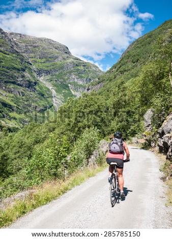Woman at Bicycle alone at an old road in the Flam valley approaching a curve With magnificent surrounding mountain view