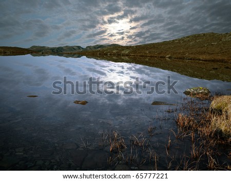 Magnificent norwegian moonlight reflection through clouds in calm water with small stones in the foreground