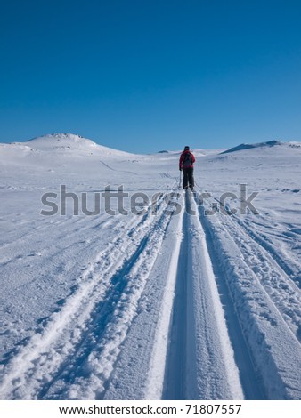 Woman skiing alone in a groomed ski track at easter towards a small mountain summit in the norwegian mountains
