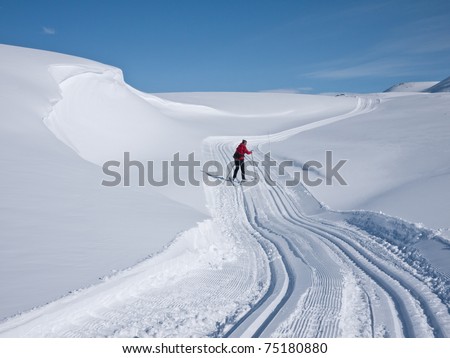 Woman skiing alone in a groomed curved double ski track with a characteristic wind swept snow formation on her left in the norwegian mountains at easter