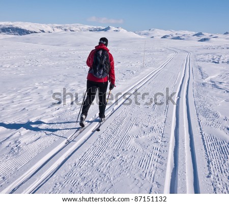 Woman skiing alone in a groomed double ski track heading towards some mountain summits in the norwegian mountains at easter