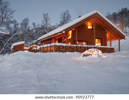 Snow covered norwegian mountain cottage during twilight hours with decoration lights in the foreground at christmas