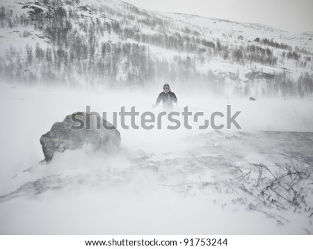 Person at ski in low visibility conditions due to a snow storm with a rock in the foreground in the norwegian mountains at winter time