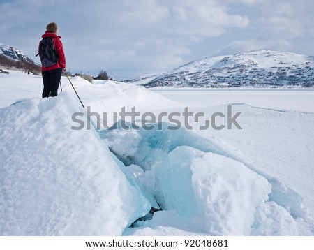 Woman at ski resting close to a snow covered lake with ice breaking up due to decrease in the water level at easter in the norwegian mountains