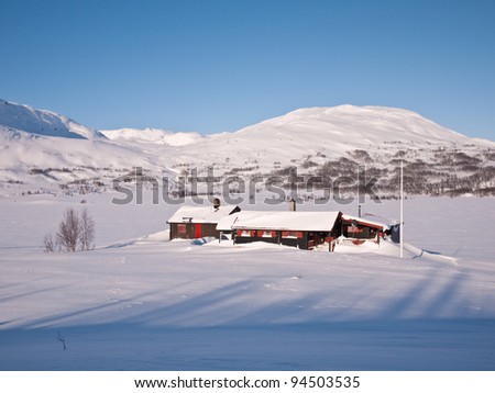 Snow covered cabin in the norwegian mountains at easter with shadows in the foreground and mountain summits in the background