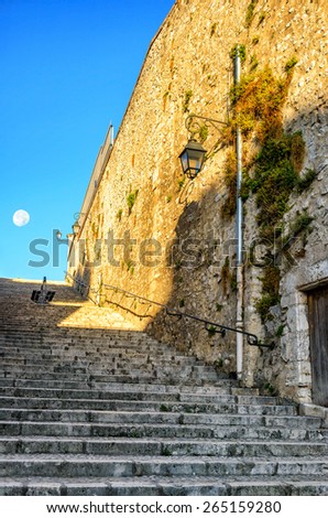 Old stone stairs and a wall on a street in the small city, France. The moon in the distance.