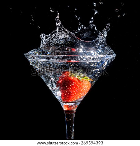 Strawberry splashing into glass of martini on a black background