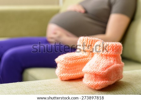 A beautiful woolen baby shoes on the couch next to a pregnant woman