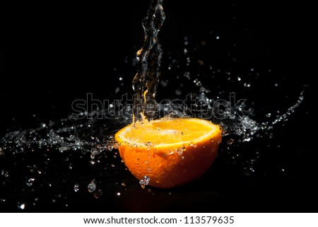 half orange with splashes of water on a black background