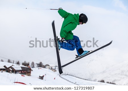 A free-ride ski jumper, with skis crossed against a mountains
