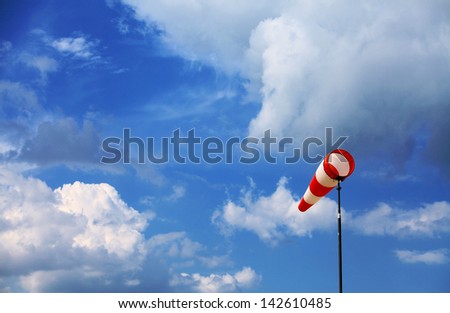 A red wind vane against a blue cloudy sky
