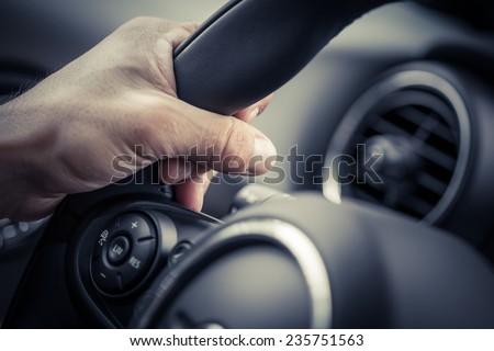 A hand pushes the cruise control button on a steering wheel.