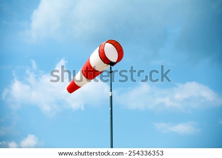 A red wind vane against a blue cloudy sky