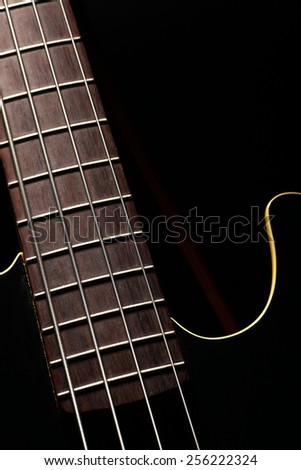 Vertical detail of the fret board of a bass guitar, on a dark background.