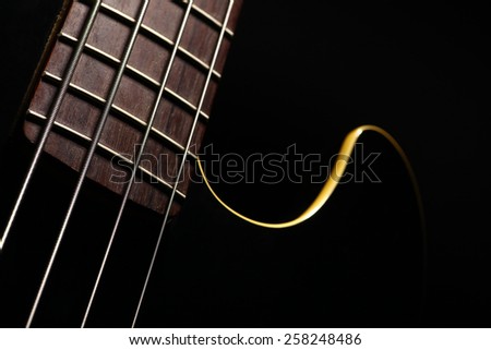 Horizontal detail of the fret board of a bass guitar, on a dark background.