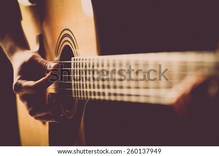 Color detail of hands playing of an old, acoustic guitar.