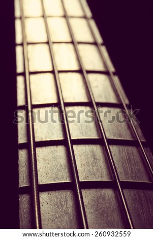 Detail of the fret board of a bass guitar, on a dark background.