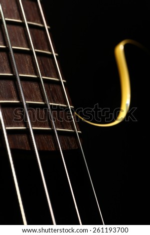 Horizontal detail of the fret board of a bass guitar, on a dark background.