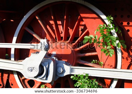 Color image of an abandoned steam locomotive\'s wheels, with plants growing around them.