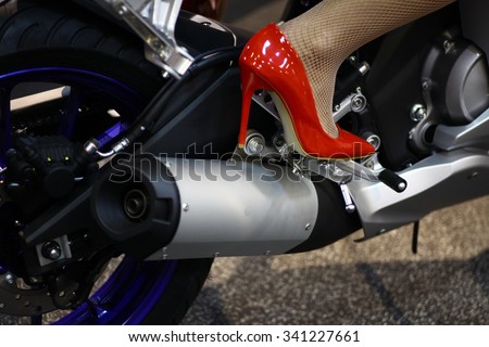 Color image of the exhaust pipes of a motorcycle and a leg of a woman, with red heels.
