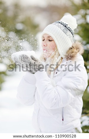 A Girl Wearing Warm Winter Clothes And Hat Blowing Snow In Winter Forest, vertical format