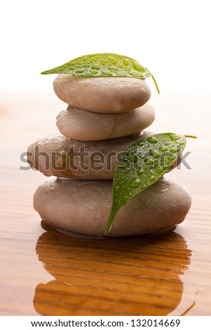 Massage stones with green leaves and water drops. Wood background.