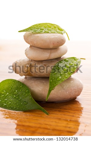 Massage stones with green leaves and water drops. Wood background.