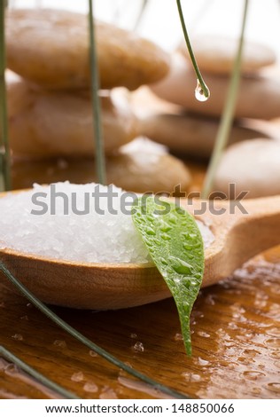 Sea salt in a wooden spoon with a green leaf, spa stones, drops of water.