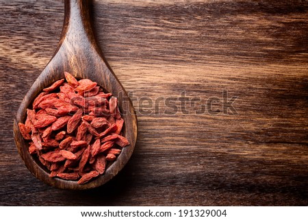 Goji berries on a wooden spoons, wooden brown background.