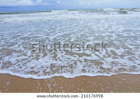 Closeup shot of foamy sea wave on sandy beach with blue-green waves rolling in background. Taken at Koh Lanta Beach, Thailand