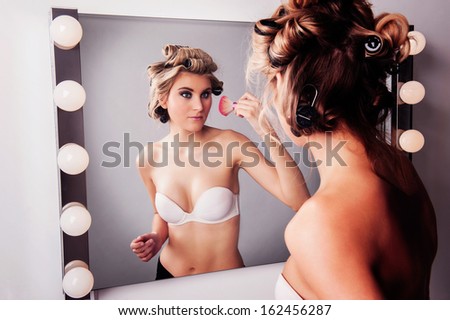 Girl applying face makeup at a studio makeup mirror.