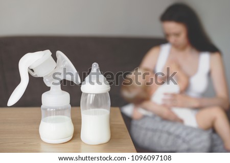 Bottle and breast pump with breast milk on the background of mother holding in her hands and breastfeeding baby. Maternity and baby care.