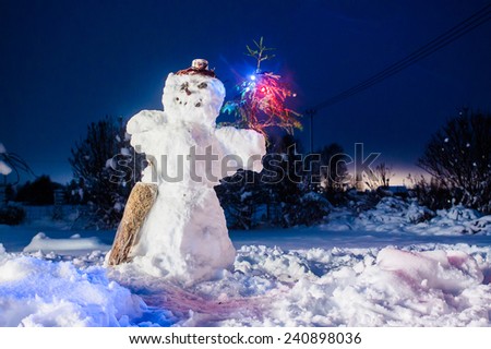 A snowman holding a lit branch of a pine tree on a yard on a dark night.