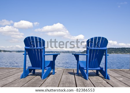 two blue chairs on a beach with beautiful view on a lake