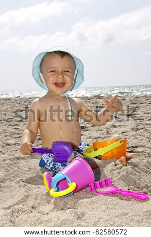 baby playing with toys  on a beach and smiling
