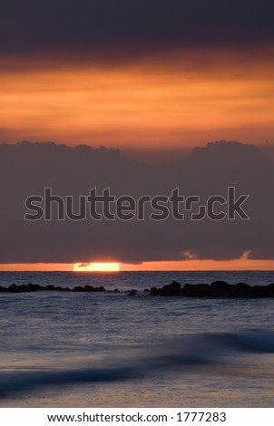 The sun sets between a layer of clouds and the ocean off Barbados.