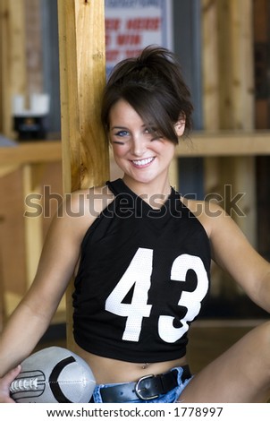 A beautiful woman in a torn football jersey and shorts.