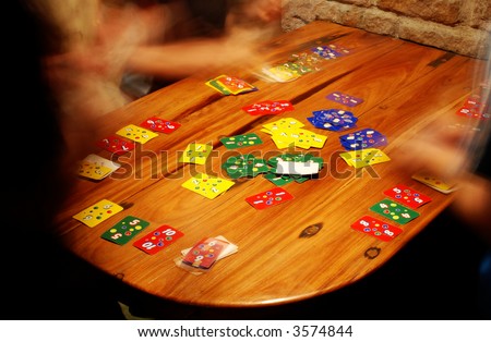 People playing a fast game of cards around a wooden table next to a stone wall