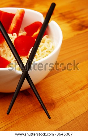 Chinese noodles with chop sticks in a bowl on wooden counter with some peppers in the noodles