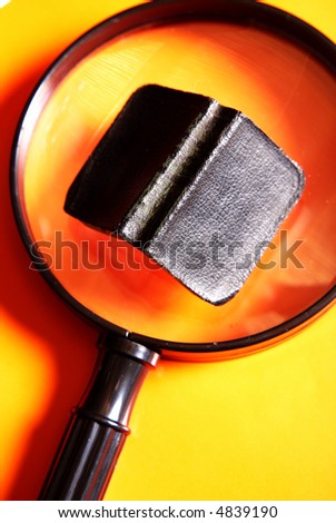 Small black book lying on a big magnifying glass on a yellow and orange background