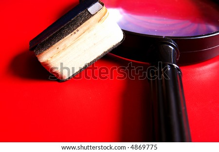 Small black book lying on a big magnifying glass on a red background