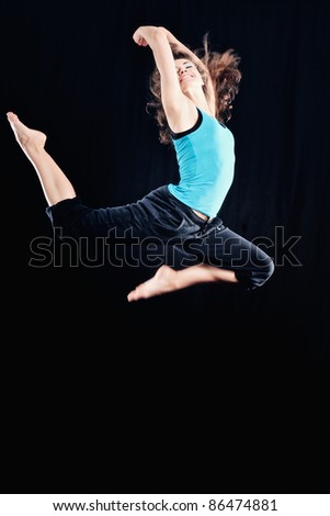 Young woman in tracksuit jumping on black background