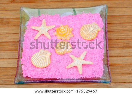 Yellow soaps with shapes of shells and starfish on pink bath salts in a glass tray