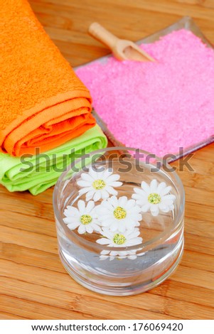 Two colorful towels next to a bowl of water with flowers on a wooden background