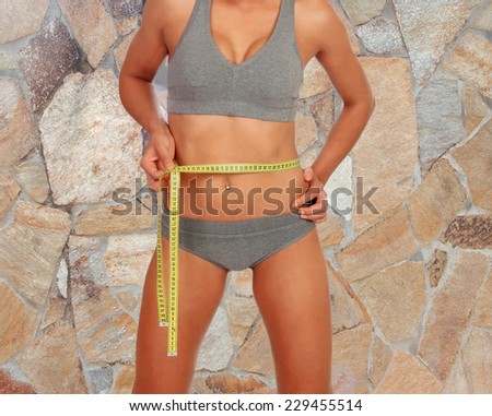 Woman with tape measuring her waist on a stone wall of background