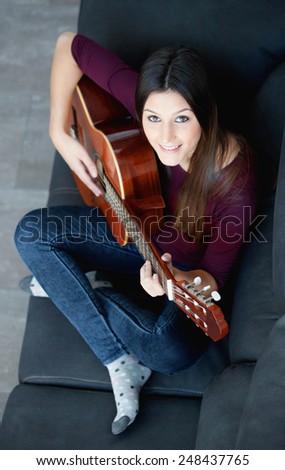 Pretty girl playing guitar on the couch at home. View from above