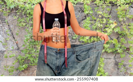 Thin woman stuck in huge pants with a water bottle and a measuring tape