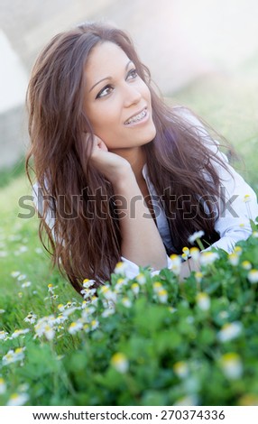 Brunette cool girl with brackets lying on the grass with many flowers