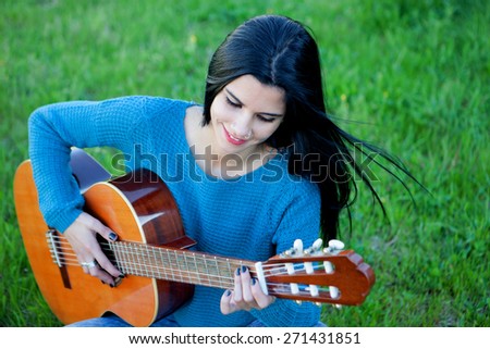 Pretty guitarist playing the guitar sitting on the grass